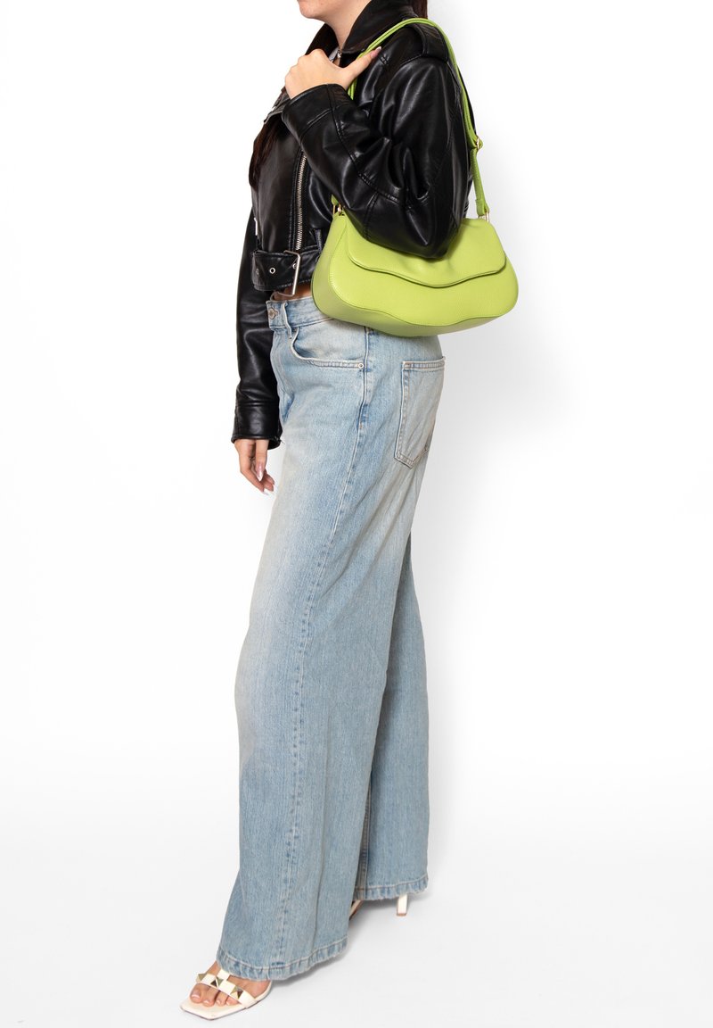 Groene, gestructureerde schoudertas met een golvend ontwerp. Draagt bij een zwart leren jasje en blauwe wijde jeans, met een casual stijl.