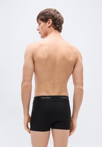 Μαύρα βαμβακερά μποξεράκια με λογότυπο στη μαύρη μέση, με εφαρμογή που αγκαλιάζει και ομαλή υφή. Το μοντέλο εμφανίζεται από πίσω.