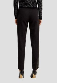 Pantaloni neri su misura, slim fit con linee pulite, caratterizzati da una texture liscia e un design classico. Abbinati a scarpe nere con tacco alto.