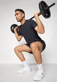 Schwarzes Sportshirt und Shorts, weiße Sneakers mit Logo, Hantel mit Gewichten heben, konzentrierte Pose, glatte Textur, minimalistisches Design.