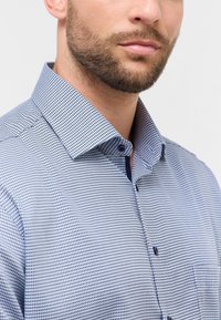 Camicia a quadri blu e bianca con colletto strutturato, tessuto testurizzato e dettaglio di una tasca sul petto.