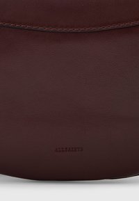 Borsa in pelle bordeaux con una texture liscia, caratterizzata da un sottile logo impressato e un design a bordi dritti. Gli accenti cuciti ne migliorano la durata.