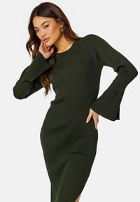 Abito a maglia a coste di colore verde scuro con maniche a campana, che presenta una vestibilità slim e uno spacco laterale per una maggiore libertà di movimento. La texture morbida aumenta il comfort.