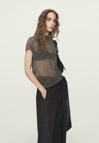 Doorschijnende grijze top met korte mouwen en een ronde hals, gecombineerd met zwarte broek met hoge taille en een strikdetail in de taille.