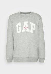 Lys grå sweatshirt med ribbet rund hals og ermer. Har stor "GAP" logo i hvitt og "Original" i rødt under. Myk tekstur.