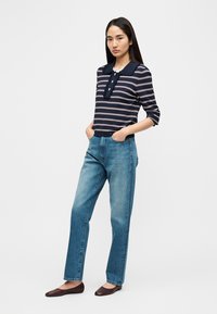 Polo rayé bleu marine et blanc avec un col et trois boutons, associé à un jean bleu clair à jambe droite et des mocassins marron foncé.