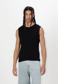 Sort ærmeløs strikket top med diamantmønster og små huller, parret med lyseblå denimshorts. Glat tekstur og tætsiddende design.