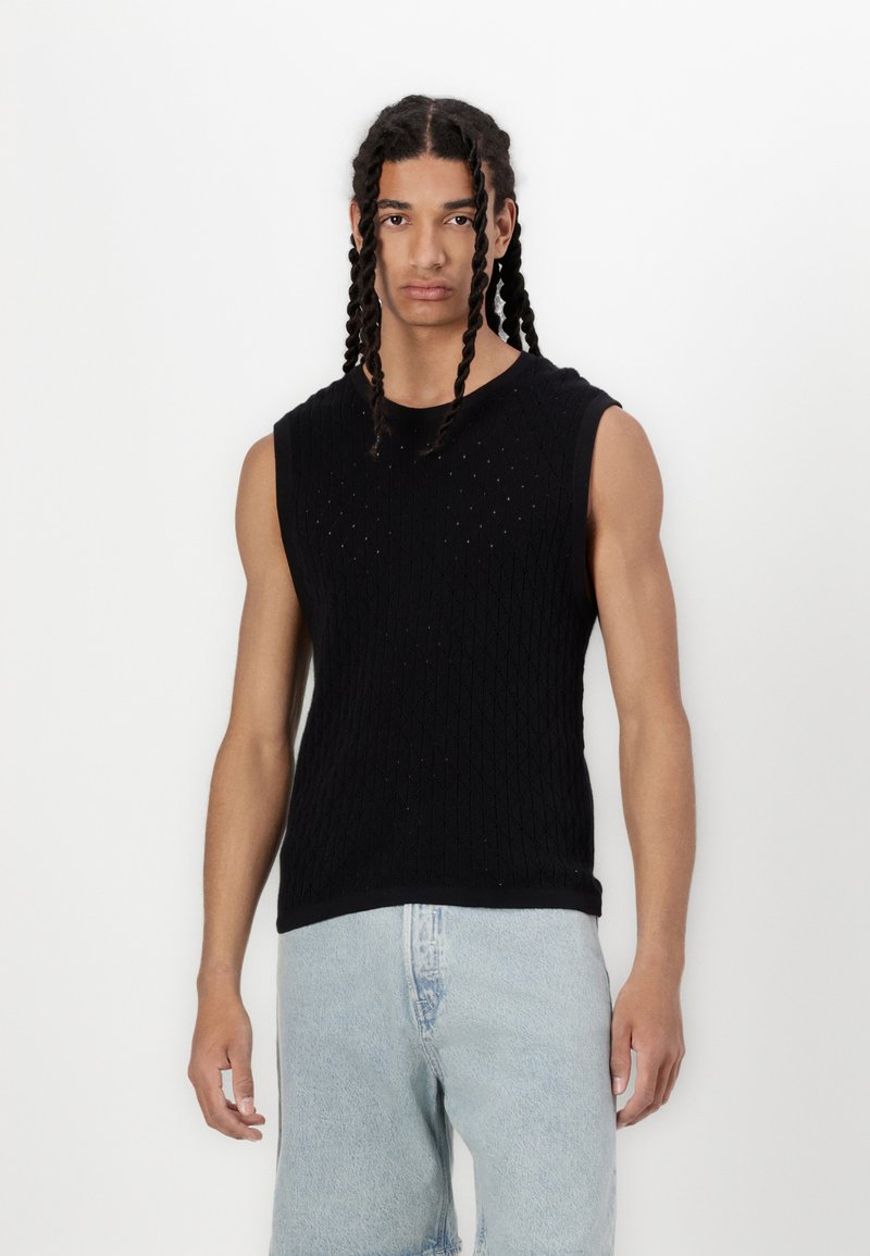 Sort ærmeløs strikket top med diamantmønster og små huller, parret med lyseblå denimshorts. Glat tekstur og tætsiddende design.