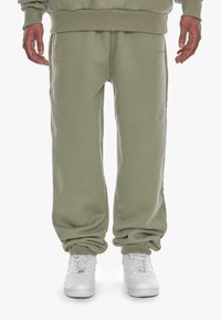 Olive green sweatpants in a soft fabric, featuring a loose fit with elastic cuffs at the ankles and a subtle logo detail on the side.