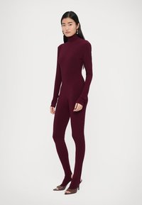 Burgundowy body z wysokim kołnierzem, długimi rękawami i dopasowanymi nogawkami. Miękki, elastyczny materiał; bezszwowy design podkreślający sylwetkę.