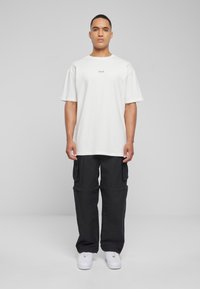 Hvit oversized t-skjorte med "loved." trykket i svart, kombinert med svarte cargo-bukser med sidelommer og hvite sneakers.