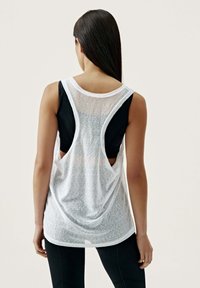 Vit, lätt ärmlös topp med genomskinlig rygg, rundad nederkant och lagerdesign över en svart tanktop. Texturerad tygyta.