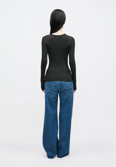 Top de mangas compridas cinza escuro com textura canelada, combinado com jeans azuis de perna larga. O conjunto apresenta mangas ajustadas e um corte descontraído nas pernas.