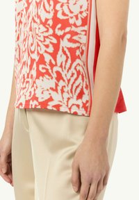 Czerwony top w kwiatowy wzór z białymi akcentami, wykonany z miękkiego materiału i w luźnym kroju, zestawiony z kremowymi spodniami.