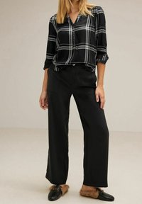 Camicia a quadri bianca e nera con maniche lunghe, abbinata a pantaloni larghi neri e pantofole nere con dettagli in pelliccia.