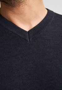 Dunkelblaues V-Ausschnitt-Pullover aus Strickstoff. Verfügt über einen gerippten Kragen und eine glatte, strukturierte Oberfläche, die den Ausschnitt betont.