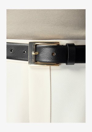 Must hele nahkvyö sileda tekstuuriga ja ruudukujuline kuldne pandla, kantud heledakarva ribadega topi ja valgete pükste kohal.