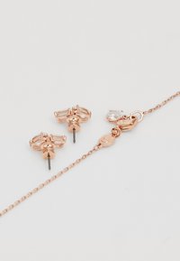Rosagulds øreringe med klare, rektangulære og runde krystaller; stud-design med kæde og spænde detaljer. Glat finish, elegant form.