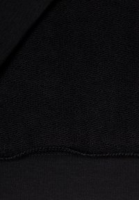 Czarny materiał tekstylny z fakturowaną powierzchnią ponad gładką, prążkowaną sekcją. Obie części są jednolicie ciemne, podkreślając prostotę wzornictwa.