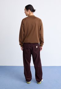 Bruine sweatshirt met een hoge kraag, gecombineerd met donkerburgundy corduroy broeken. De broeken hebben achterzakken en een merktag.