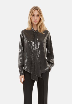 Blouse noire brillante en sequins avec un col à bouton et un détail de nœud, dotée de manches longues et d'une coupe décontractée.