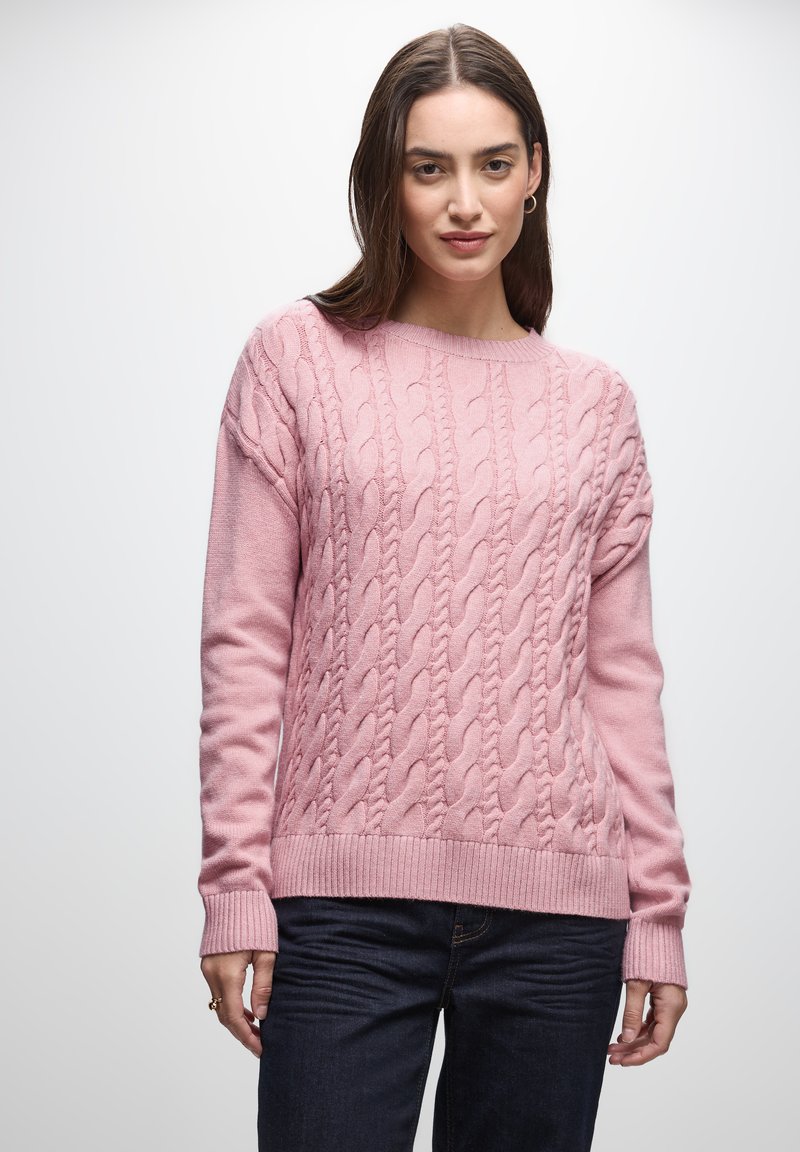 Roze kabelgebreide trui met lange mouwen, een geribde halslijn en zoom, en een zachte textuur. Gecombineerd met donkerblauwe jeans voor contrast.