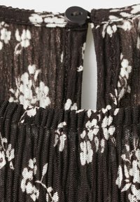 Prim-plan cu țesătură neagră cu imprimeu floral alb, prezentând nervuri texturate, detaliu elastic și închidere cu nasture negru în partea de sus.