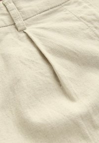 Light beige linen fabric with a subtle texture and pleated design. Features a flat waistband and natural fiber appearance.