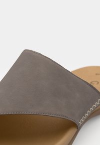 Sandalo a scivolo in pelle grigia con una larga fascia, dettagli cuciti e una soletta beige testurizzata. Design semplice con punta aperta e retro scoperto.