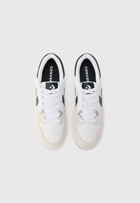 Bijele i bež tenisice s gornjim dijelom od brušene kože i kože, crnim akcentima i ravnim vezicama. Zvjezdani logo na jeziku; perforirani vrh za ventilaciju.