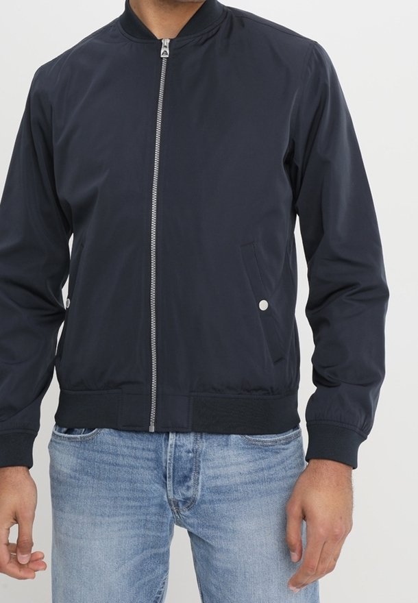 Chaqueta bomber de color navy con cuello alzado, cremallera frontal y bolsillos laterales. Tejido liso con puños y dobladillo acanalados.