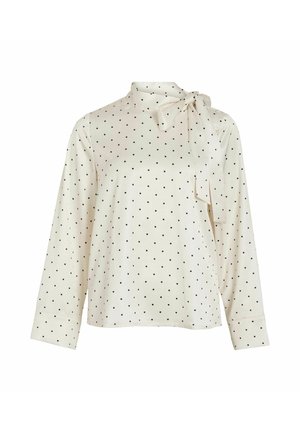 Blouse crème à manches longues avec pois noirs, col montant et détail nœud. Texture lisse et coupe décontractée, manches ajustées avec poignets.