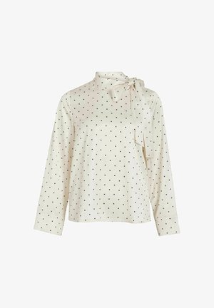 Blouse crème à manches longues avec pois noirs, col montant et détail nœud. Texture lisse et coupe décontractée, manches ajustées avec poignets.