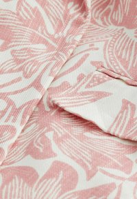 Blumenmusterstoff, der in Rosa und Cremefarben gehalten ist und eine strukturierte Oberfläche aufweist. Das Design umfasst Blätter und fließende Linien, die einen dynamischen Look erzeugen.