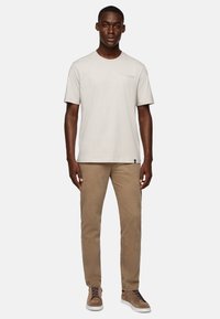 Light gray cotton t-shirt with short sleeves, featuring a subtle pocket detail. Paired with tan corduroy pants and brown sneakers.