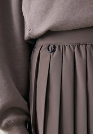Brun plisserad kjol med en mjuk textur, med en svart cirkulär detalj på midjebandet, tillsammans med en matchande brun sweatshirt.