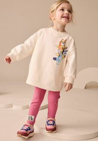 Felpa crema con grafica di un cane dei cartoni animati, abbinata a leggings rosa a costine e sneaker multicolori con dettaglio di un patch a forma di cane.