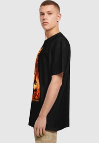 Black oversized t-shirt featuring a vibrant flame graphic, short sleeves, and a round neckline, made from soft cotton material.