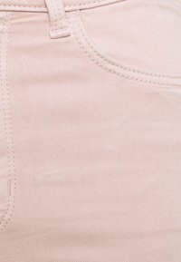 Tejido de mezclilla rosa claro con patrón de tejido diagonal, que presenta un bolsillo visible y detalles de costura. Textura suave con un ligero brillo.