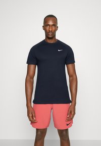 Marineblå trenings t-skjorte med korte ermer og rund hals, med en hvit Nike-logo på venstre bryst. Glatt stofftekstur.