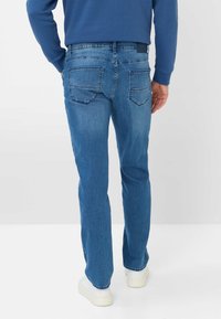 Jeans in denim blu con taglio dritto, dotati di due tasche posteriori e di una leggera scoloritura. Indossati con sneakers bianche e una felpa blu.