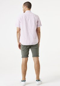 Korte mouwen lichtroze shirt van textuurstof, opgerolde mouwen, olijfgroene shorts en witte sneakers met groene accenten.