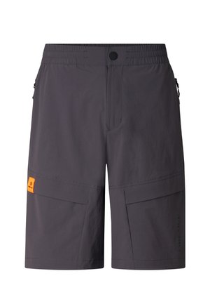 Mann trägt schwarzen Hoodie, graue Cargoshorts, schwarze Sneakers, Sonnenbrille, hält einen schwarzen Rucksack an einem Träger vor einfarbigem Hintergrund.
