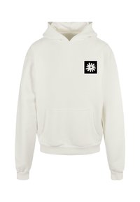Sudadera blanca con capucha y bolsillo frontal, que presenta un cuadrado negro con un gráfico de una flor blanca en la zona del lado izquierdo del pecho. Textura de tela suave.