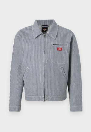 Veste zippée pour homme à rayures bleues et blanches avec col, deux poches avant et un écusson rouge sur la poche poitrine gauche.