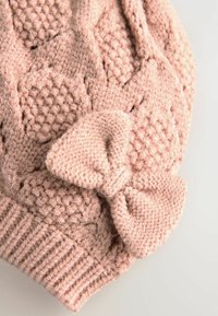 Bonnet tricoté rose avec un motif texturé à hexagones en relief et un grand nœud sur le côté. Laine douce et bande côtelée.