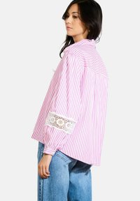 Pink and white striped shirt with long sleeves featuring lace accents at the cuffs. Loose fit with a back yoke detail and rounded hem.
