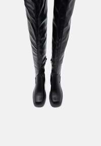 Černé kožené vysoké boty až ke kolenům se štíhlým designem, čtveratou špičkou, vnitřními zipy a hladkým povrchem. Vhodné pro různé styly.