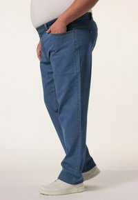 Jeans de mezclilla azul con corte recto, que cuentan con un diseño clásico de cinco bolsillos, passadores para cinturón y cierre de cremallera. Llevados con zapatillas blancas.