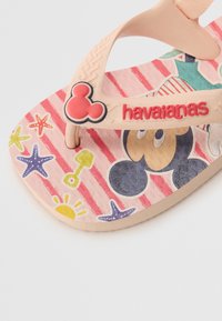 Chinelo Havaianas com uma sola listrada em rosa, decorada com padrões coloridos de estrelas-do-mar e sol, um design do Mickey Mouse em preto e bege, e uma tira de borracha macia.